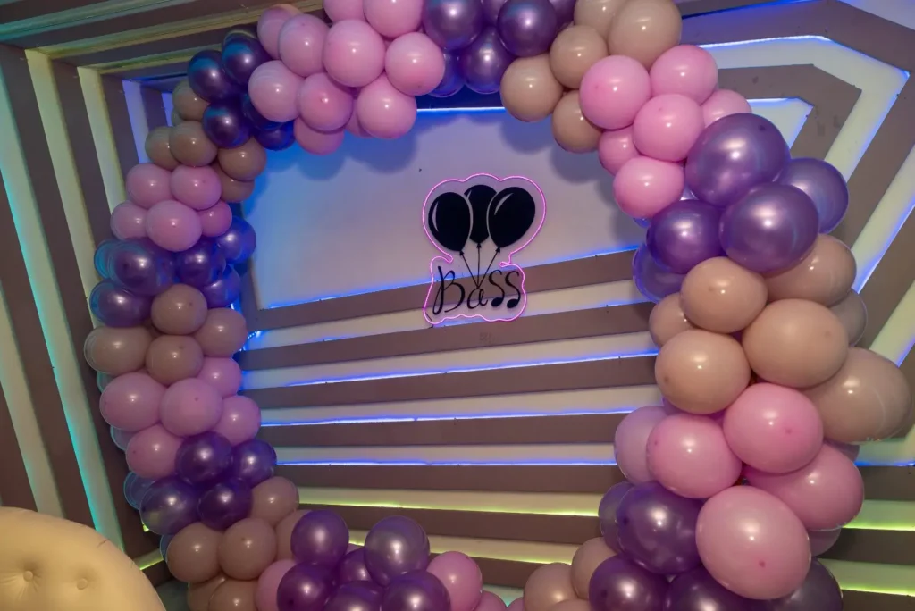 Arco de globos en tonos morados con el logotipo de Bass frente al muro LED