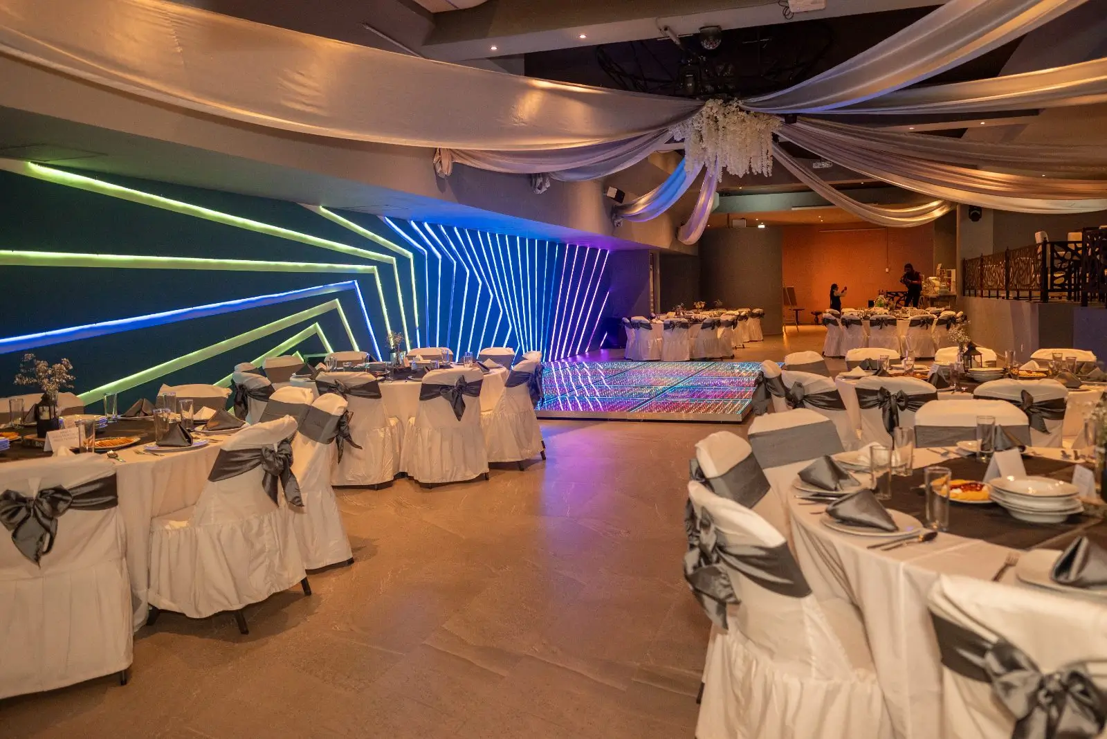 Salón montado con mesas y sillas vestidas mientras el muro LED ilumina el fondo en verde y azul